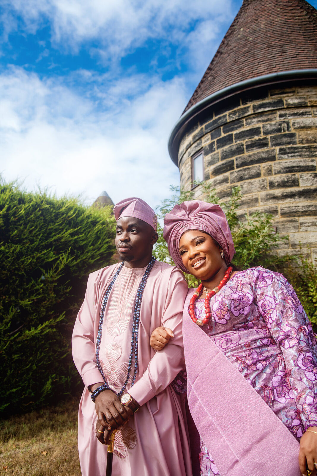 A couple in lilac aso-oke by a stone chapel tower, Wadhurst